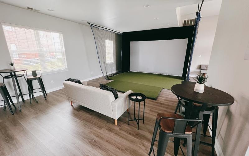 a golf simulator with a couch chairs and table